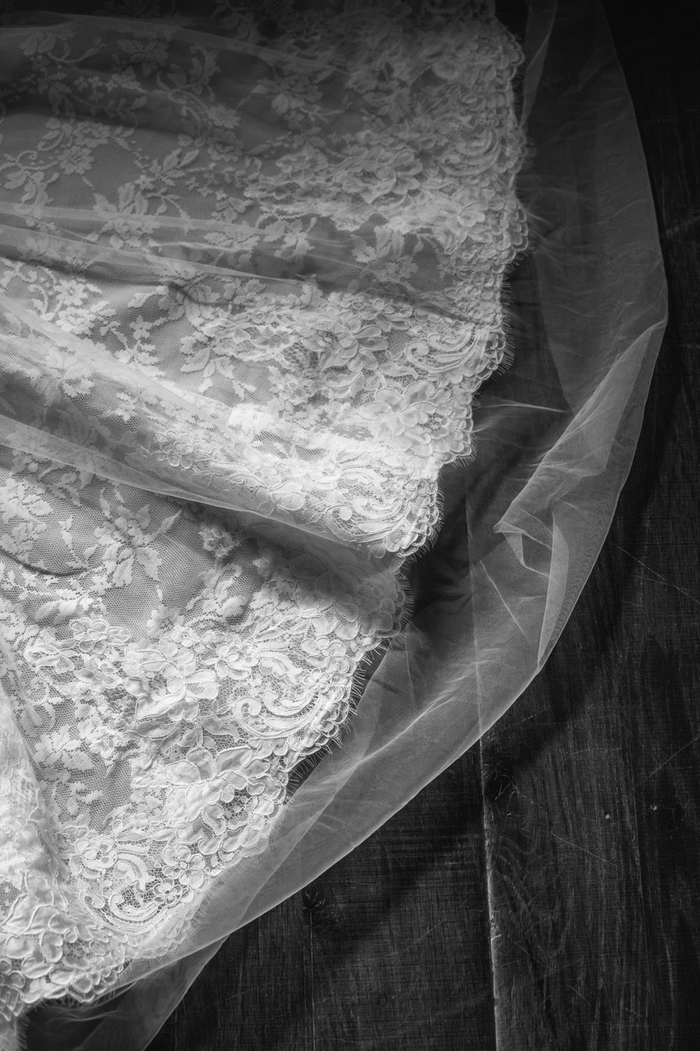 Black and white close-up detail of intricate lace embroidery on a bridal wedding gown with sheer tulle overlay.