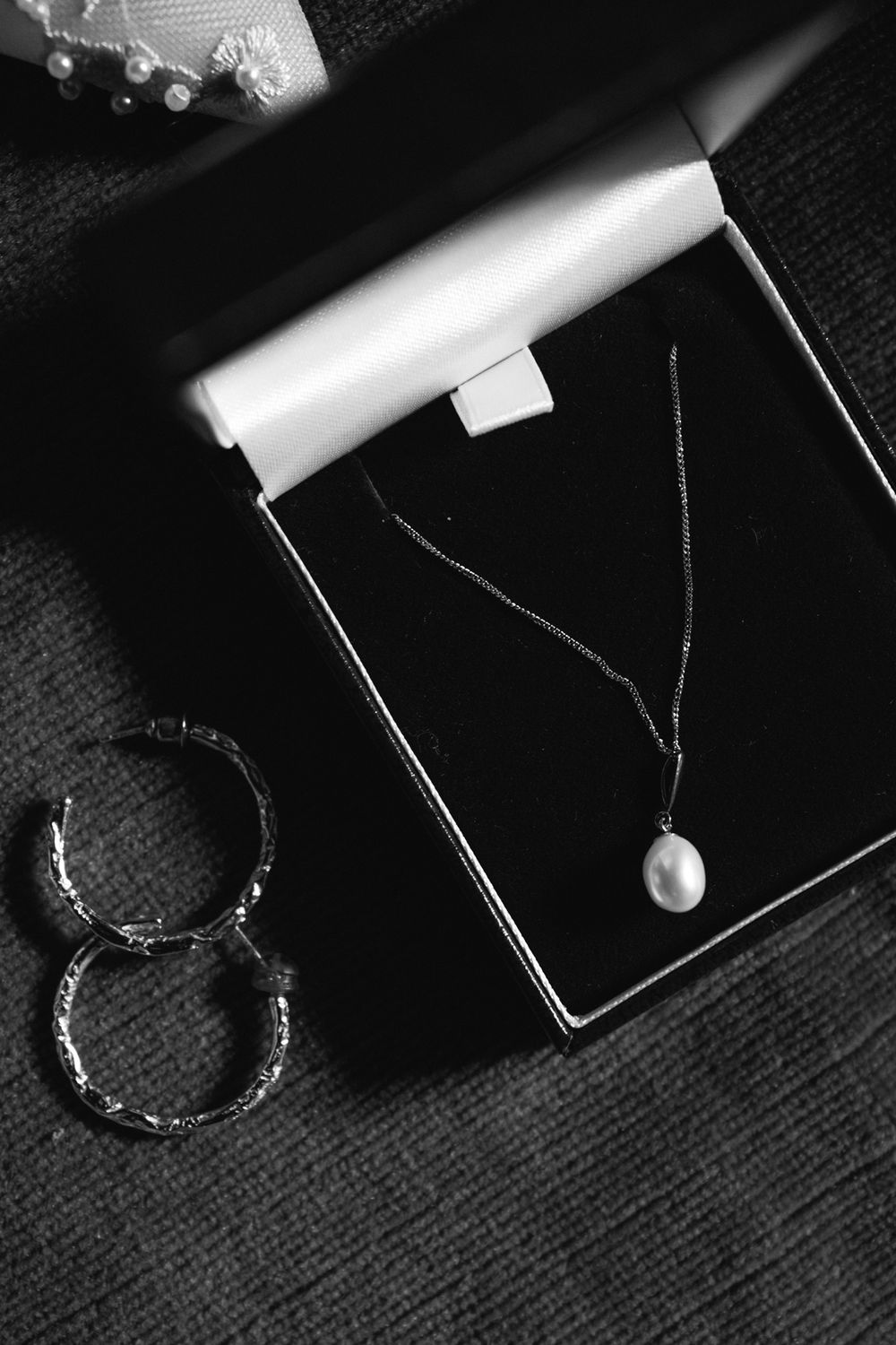 Pearl pendant necklace in black jewelry box with silver hoop earrings beside it.