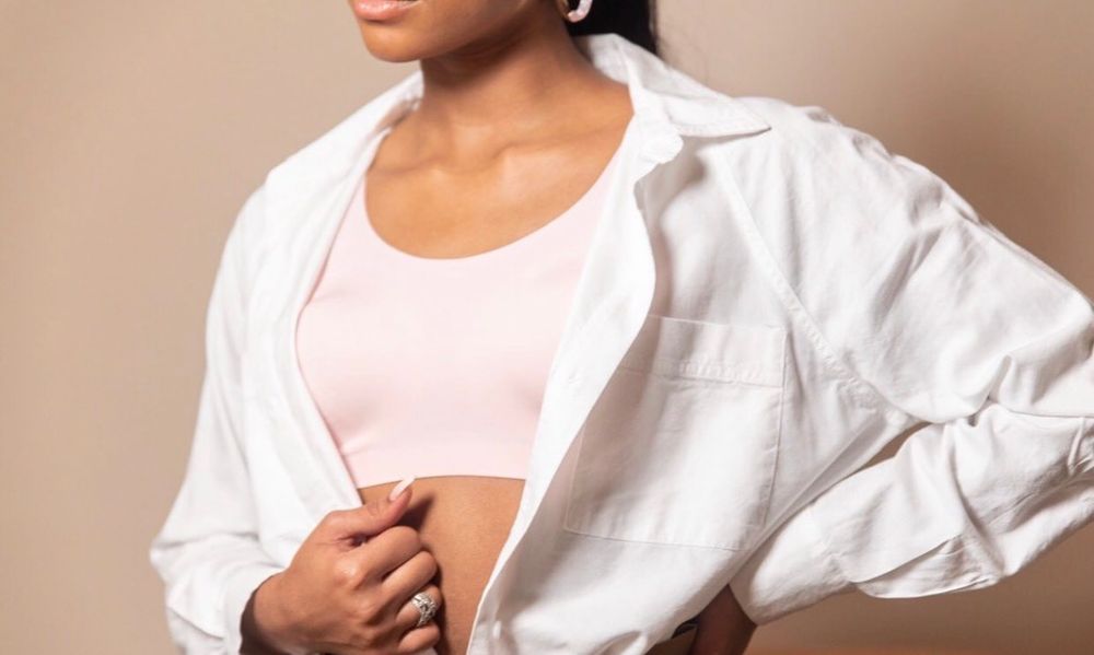 Woman in white open shirt over pink crop top posing against beige background.
