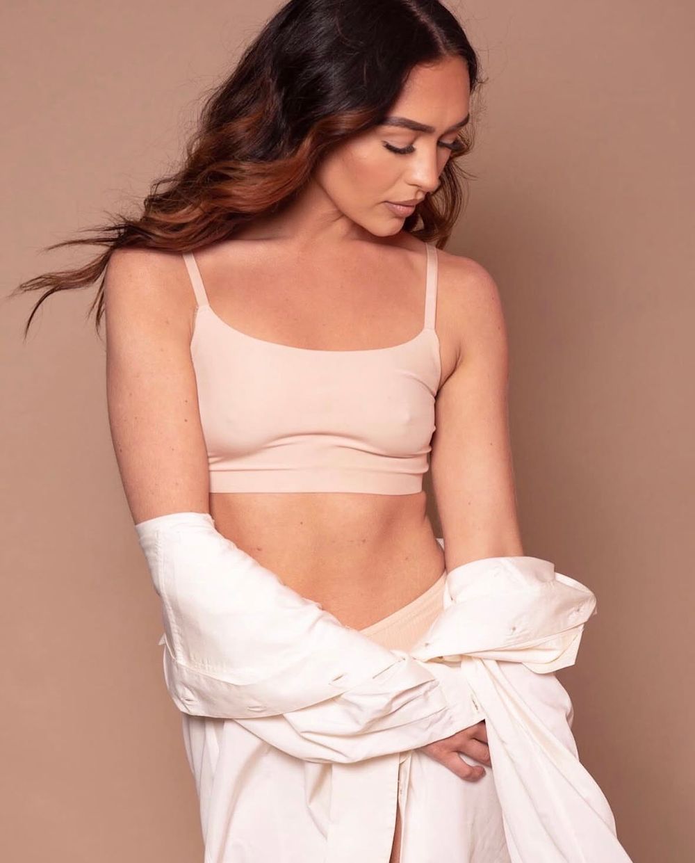 Woman posing in a nude pink sports bra crop top with a white shirt draped over her shoulders.