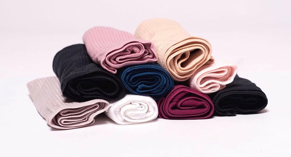 Collection of colorful ribbed fabric rolls in pink, black, navy, burgundy, and beige arranged on white surface.