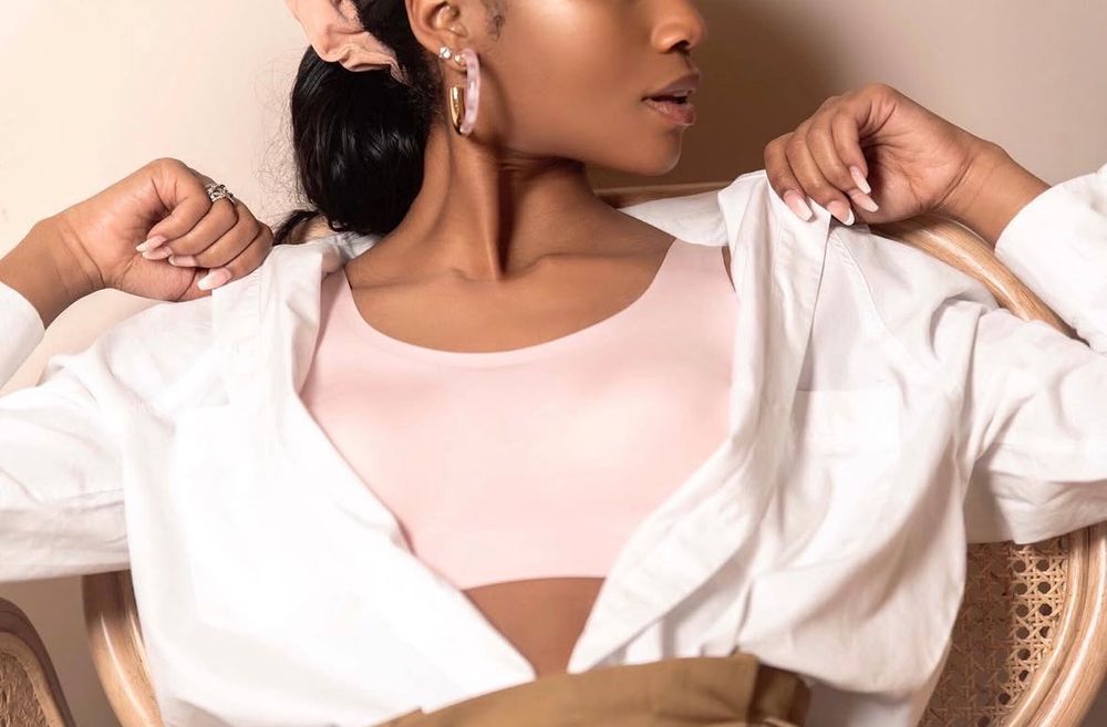 Woman in white open shirt revealing a pink bodysuit while sitting in a wicker chair.