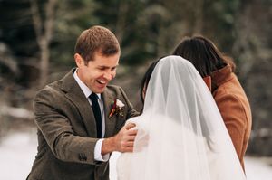 Groom smiles warmly at bride during snowy winter wedding ceremony outdoors.