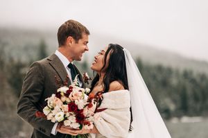 Bride and groom sharing romantic moment holding bouquet of red and white flowers in winter setting.