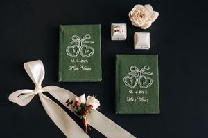 His and hers green velvet vow books with embroidered hearts displayed on dark background with florals.