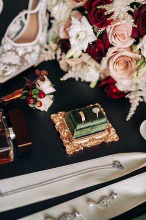 Elegant wedding flat lay with diamond ring in green velvet box, red roses, and bridal accessories.