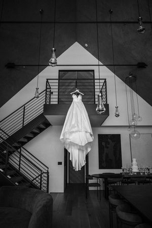 Black and white photo of a wedding dress hanging in a modern industrial venue with pendant lights.