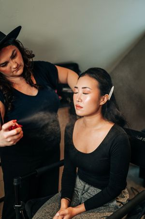 Makeup artist spraying setting spray on Asian bride during wedding preparation in studio.