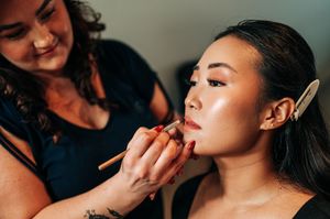 Makeup artist applies lipstick to bride during professional bridal beauty preparation session.
