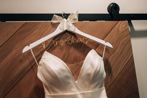 Custom wire Mrs. Shaw name hanger with ivory satin wedding dress on rustic wood barn door.