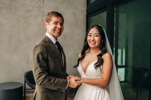 Smiling bride and groom exchange rings during wedding ceremony, bride in white gown with veil, groom in gray suit.