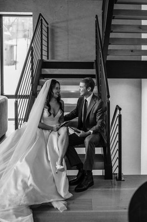 Black and white photo of bride and groom sitting on modern staircase sharing vows.