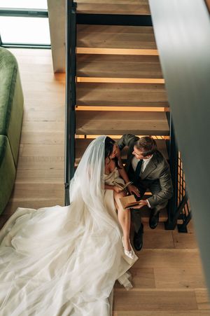 Overhead view of bride in white gown and groom reading on wooden staircase.