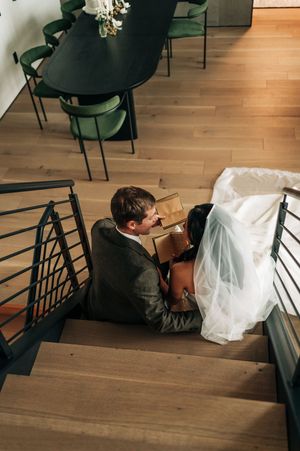 Aerial view of bride and groom sitting on modern staircase reading a book together indoors.