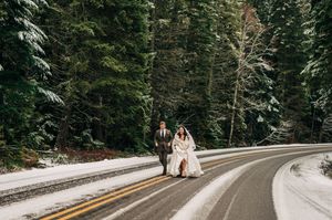 Bride and groom walk hand in hand on snowy forest road during winter wedding.