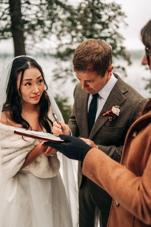 Bride and groom sign wedding documents outdoors in winter, officiant holding registry book.