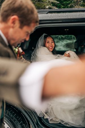 Joyful bride in white veil laughs inside vehicle during winter wedding day celebration.