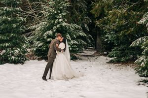 Bride and groom share a tender kiss surrounded by snow-covered evergreen trees in winter.