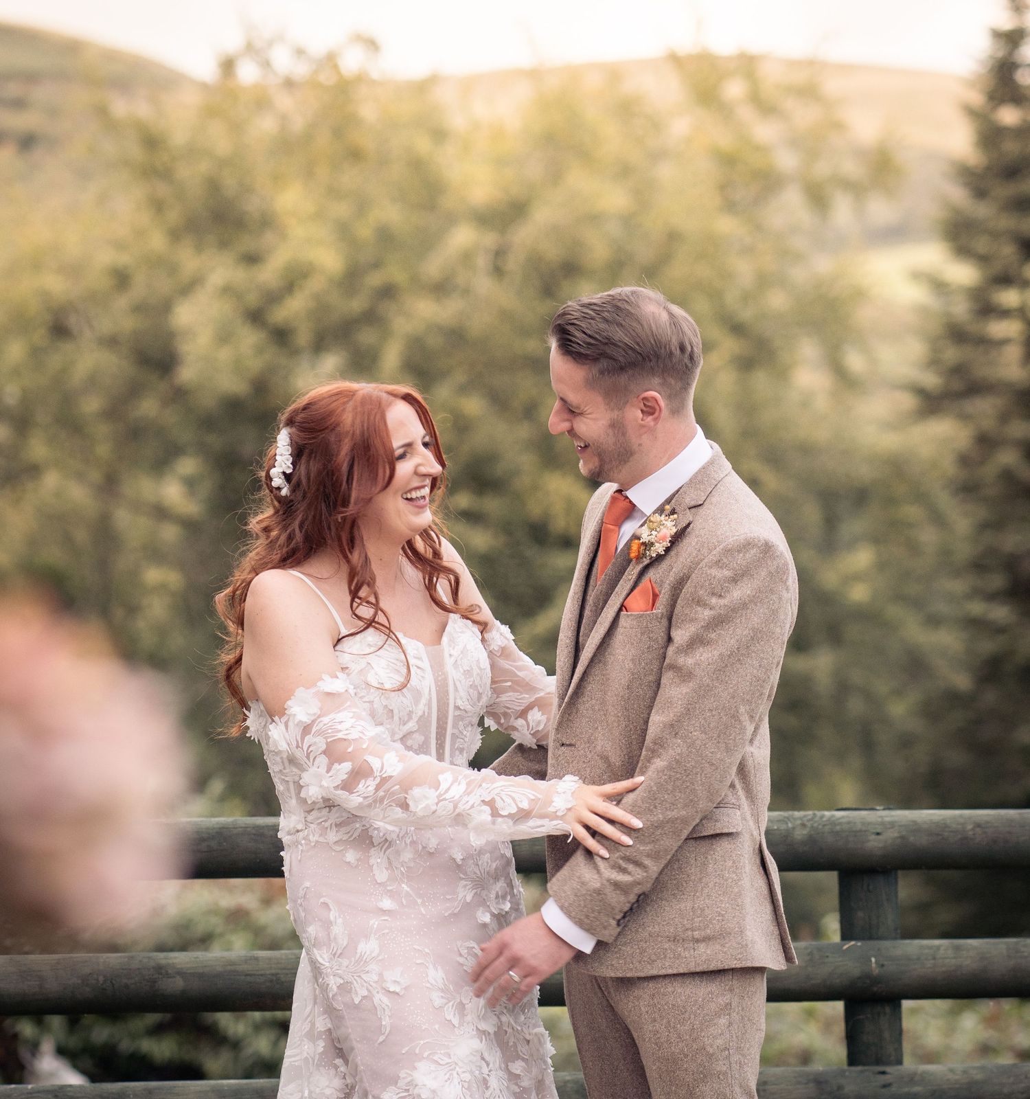 A couple shares a tender moment together at a scenic overlook with trees in the background during golden hour.