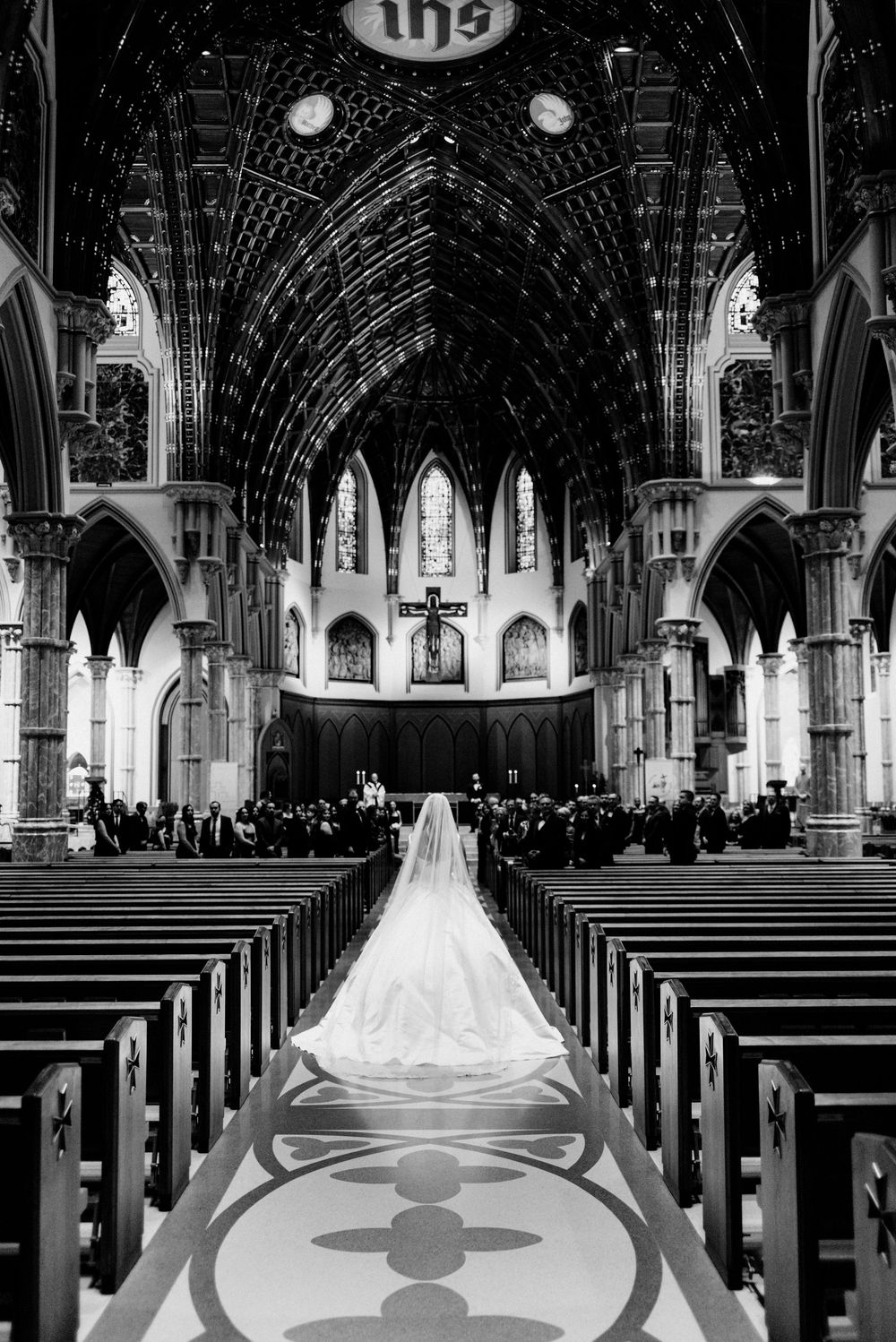 Black and white photo of a bride walking down the aisle of the Gothic Holy Name Cathedral during Catholic wedding ceremony.