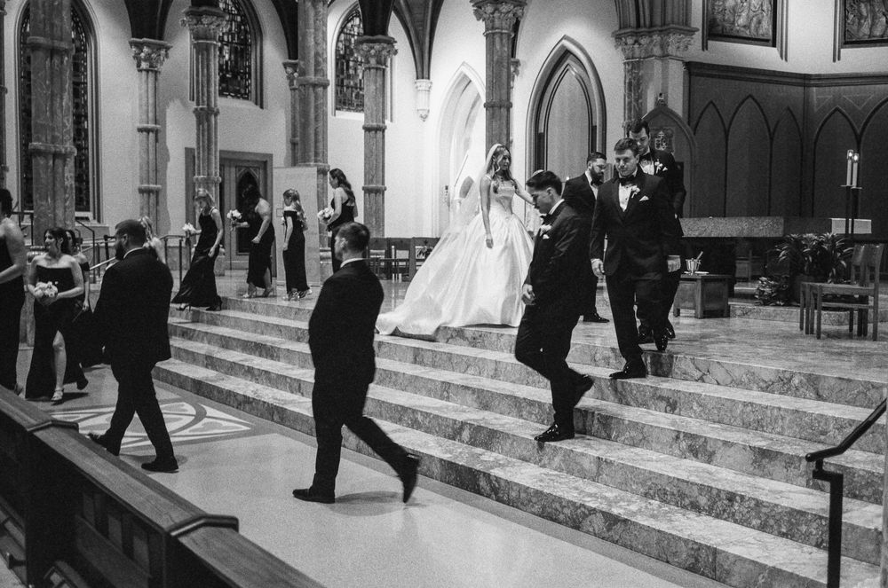 Wedding party descends marble altar steps in elegant Gothic church during ceremony in monochrome photo.
