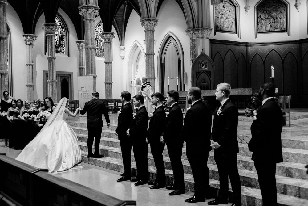 Black and white photo of a bride and groom at the altar with groomsmen standing in a grand Gothic church.