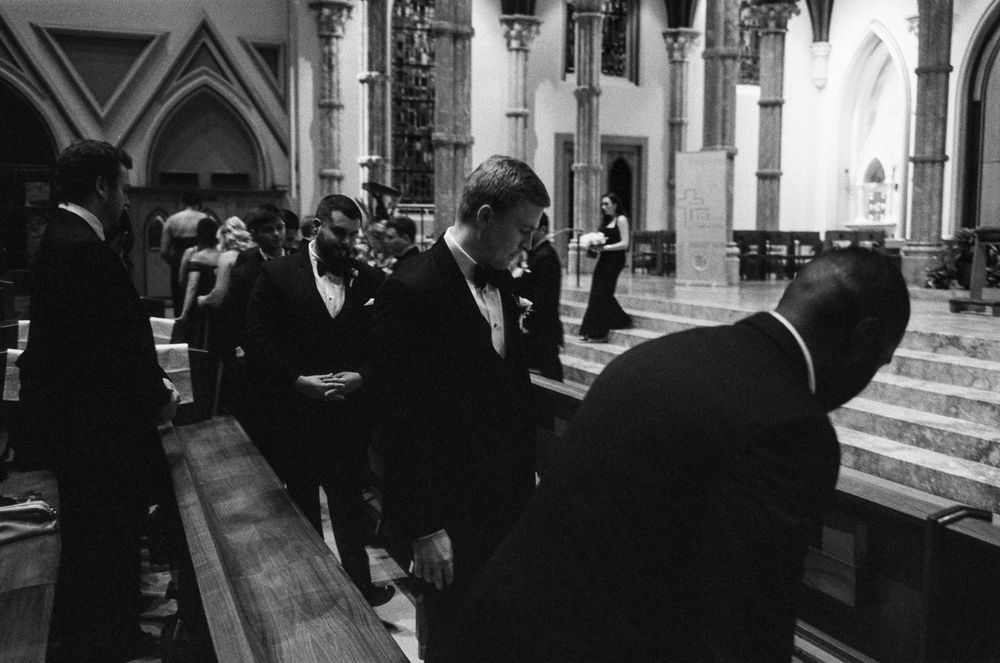 Black and white photo of groomsmen bowing respectfully at church pew during a formal wedding ceremony.