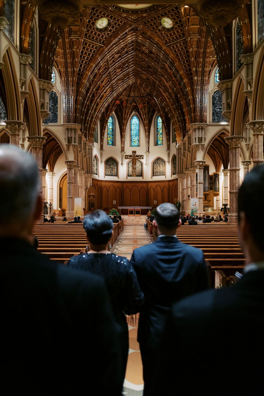 Guests standing in ornate Gothic cathedral aisle during Midwest Catholic wedding ceremony with stunning Gothic architecture.