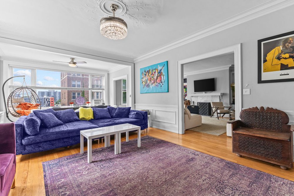 Bright living room with blue velvet sectional, purple rug, hardwood floors, and colorful art leading to an adjacent sitting room. Detroit Mi