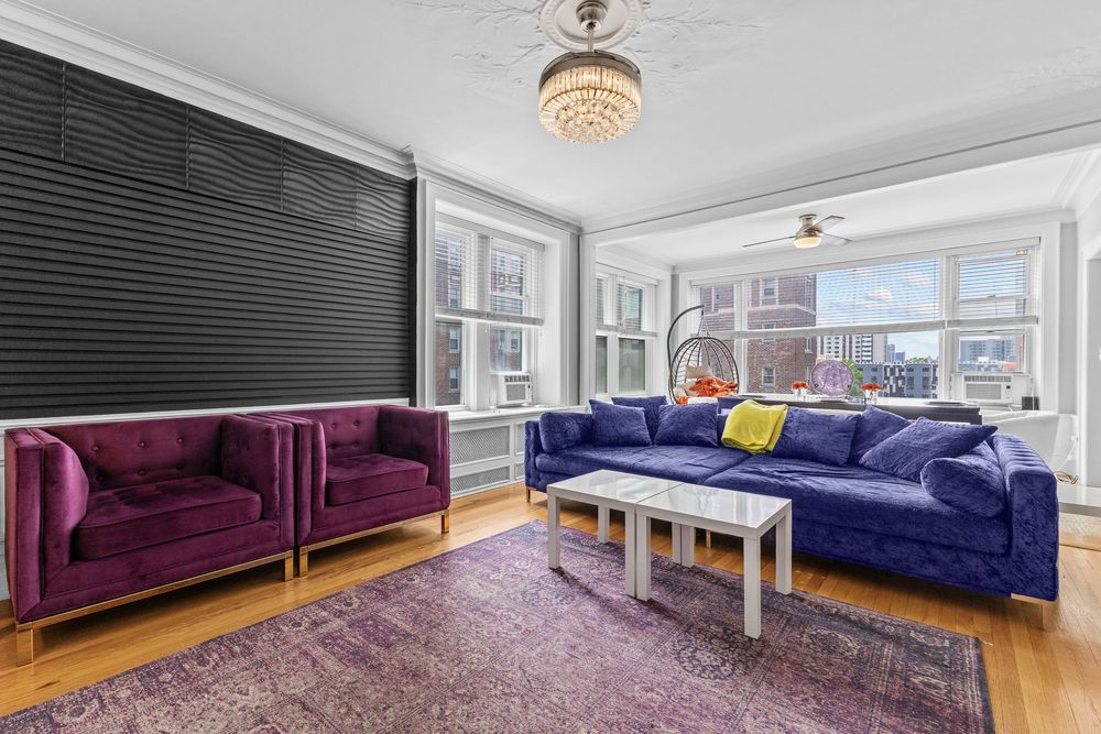 Colorful living room with purple velvet sofa, blue couch, chandelier, hardwood floors, and large windows. Detroit Michigan