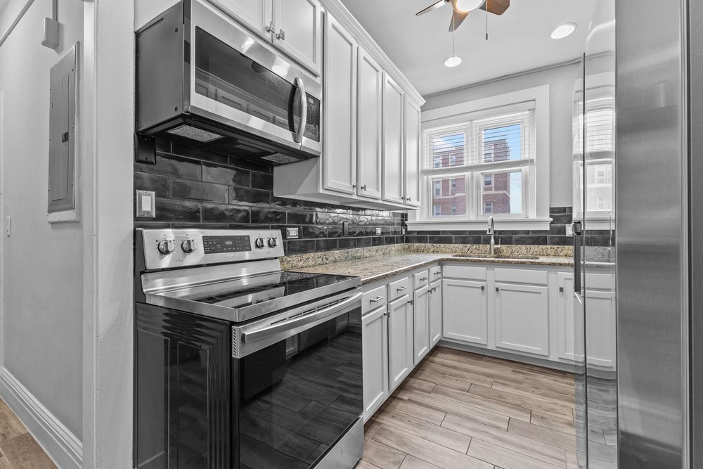 Modern kitchen with white cabinets, stainless steel appliances, dark tile backsplash, and light wood floors. Detroit Michigan