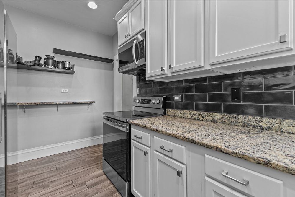 Modern kitchen with white cabinets, granite countertops, stainless steel appliances, and dark subway tile backsplash. Detroit Michigan