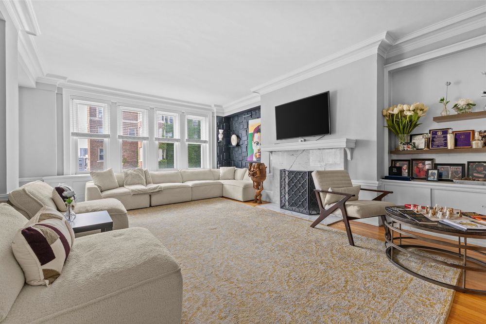Elegant living room with crown molding, white sectional sofa, marble fireplace, built-in shelves, and hardwood floors. Detroit Michigan