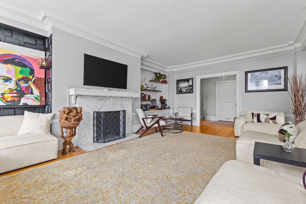 Elegant living room with marble fireplace, crown molding, hardwood floors, and white sofas atop a decorative area rug. Detroit Michigan