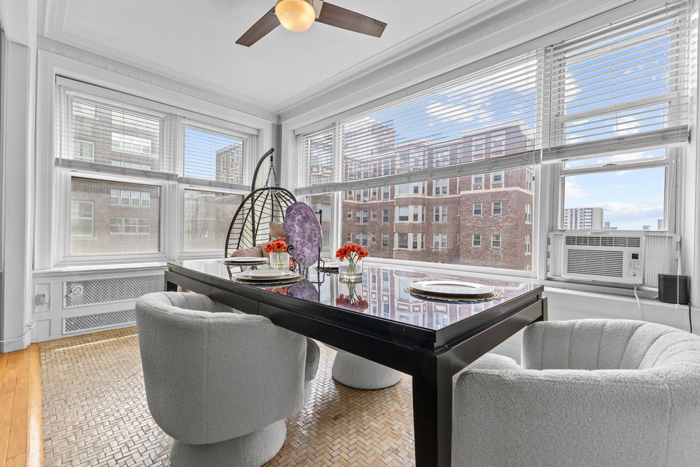 Bright sunroom with floor-to-ceiling windows, modern black dining table, gray chairs, ceiling fan, and city building views. Detroit Michigan