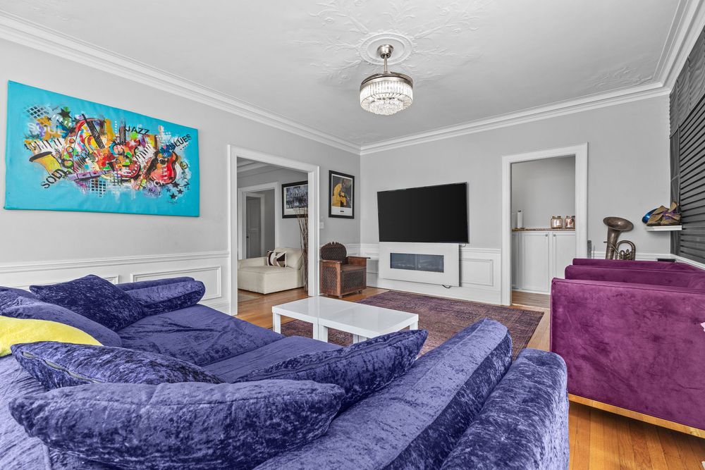 Living room with blue velvet sectional sofa, colorful wall art, wall-mounted TV, and hardwood floors. Detroit Michigan
