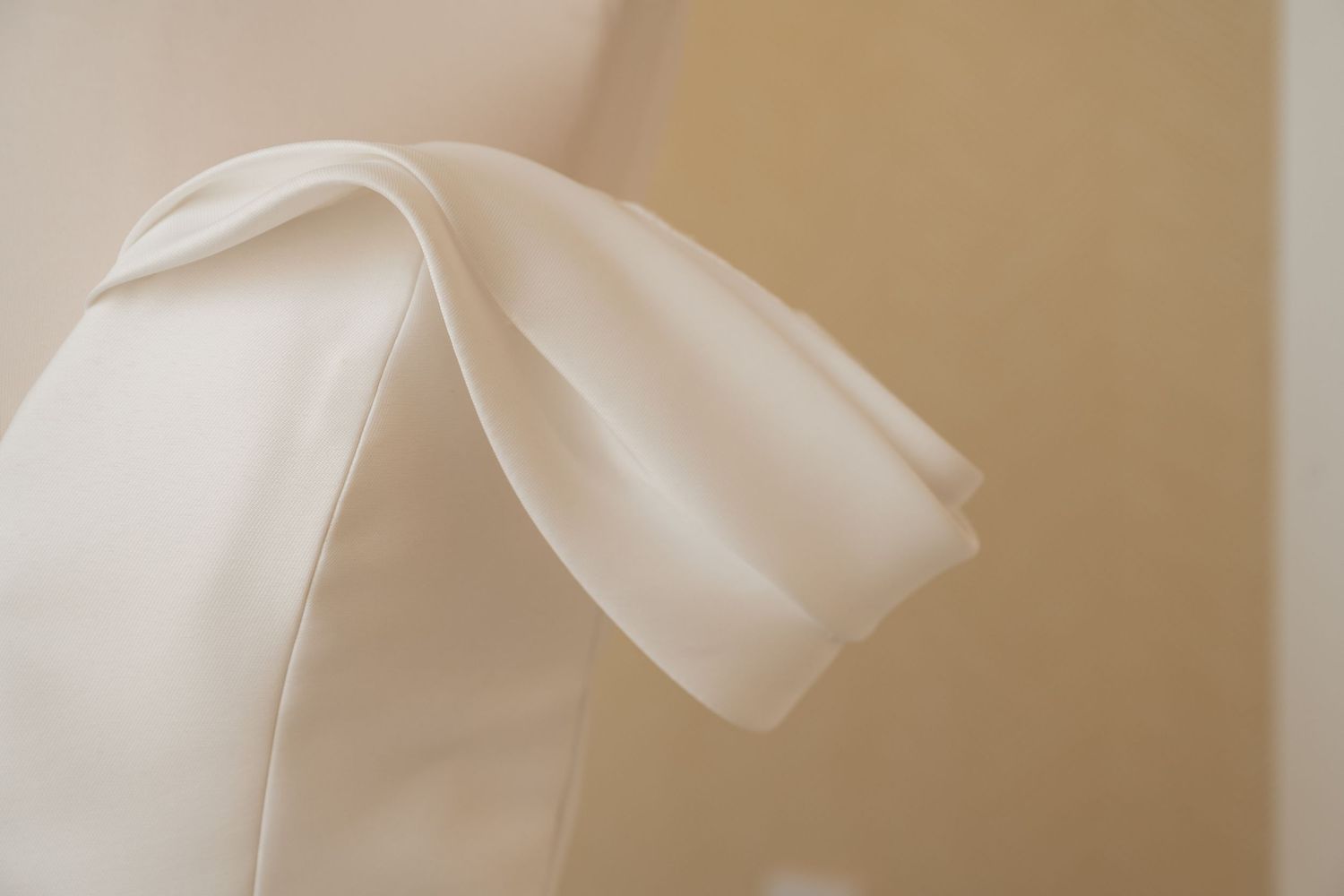 Close-up of elegant ivory satin fabric with soft draped folds against a neutral background.