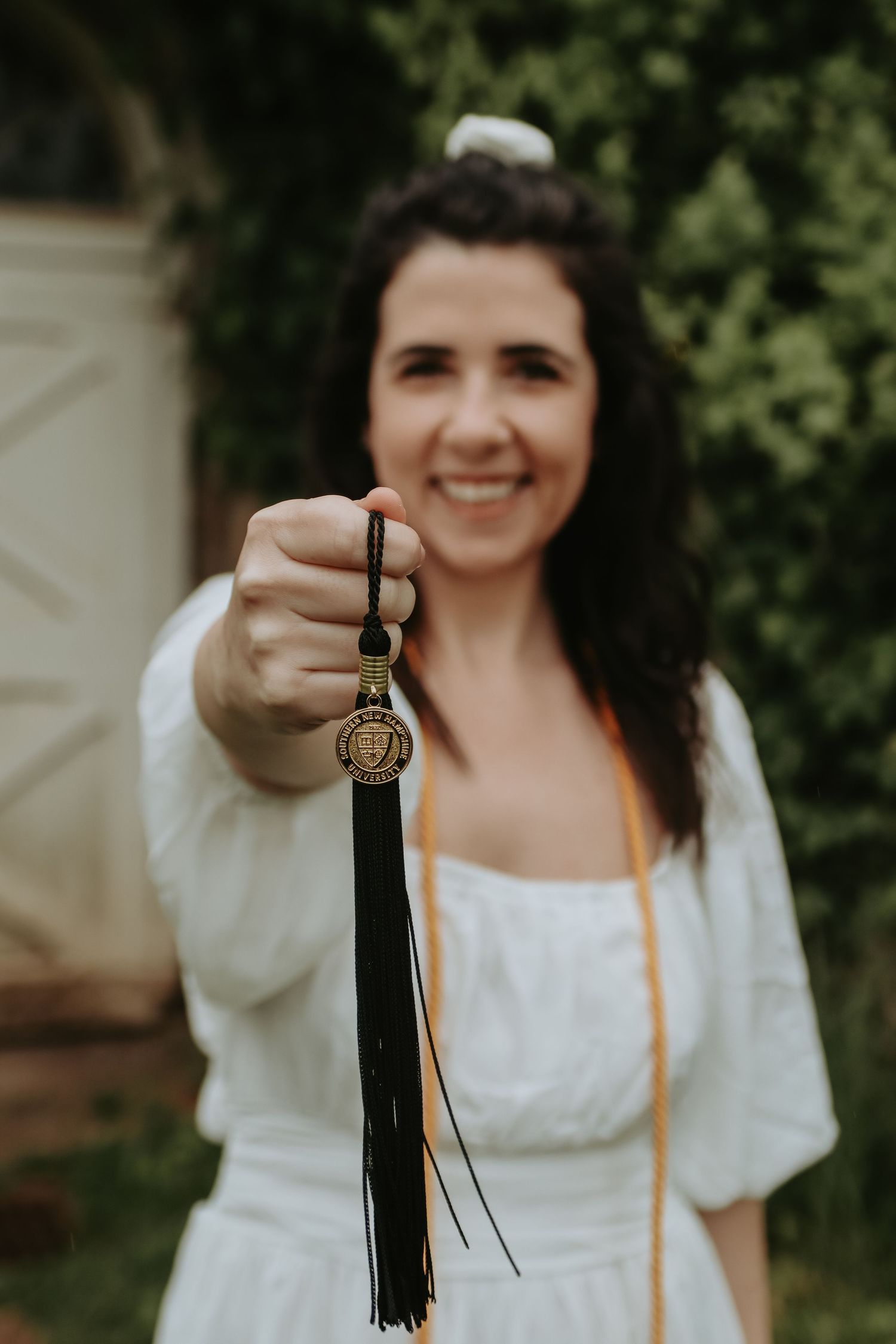 A person in a white dress holds up graduation tassel against a dark green background.