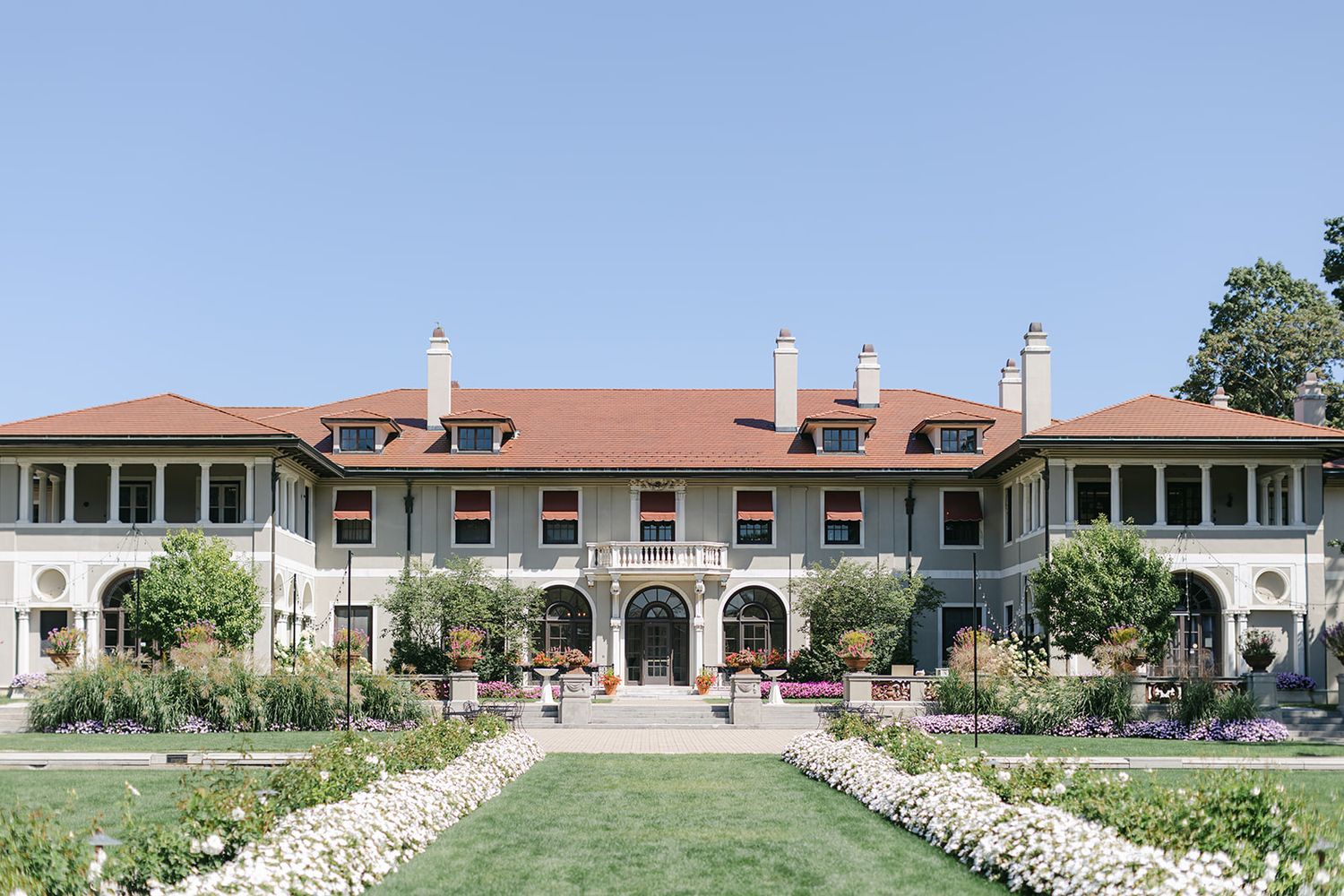 Armour House Wedding - Elegant historic mansion with red tile roof, manicured gardens, and white flower borders under a clear blue sky.