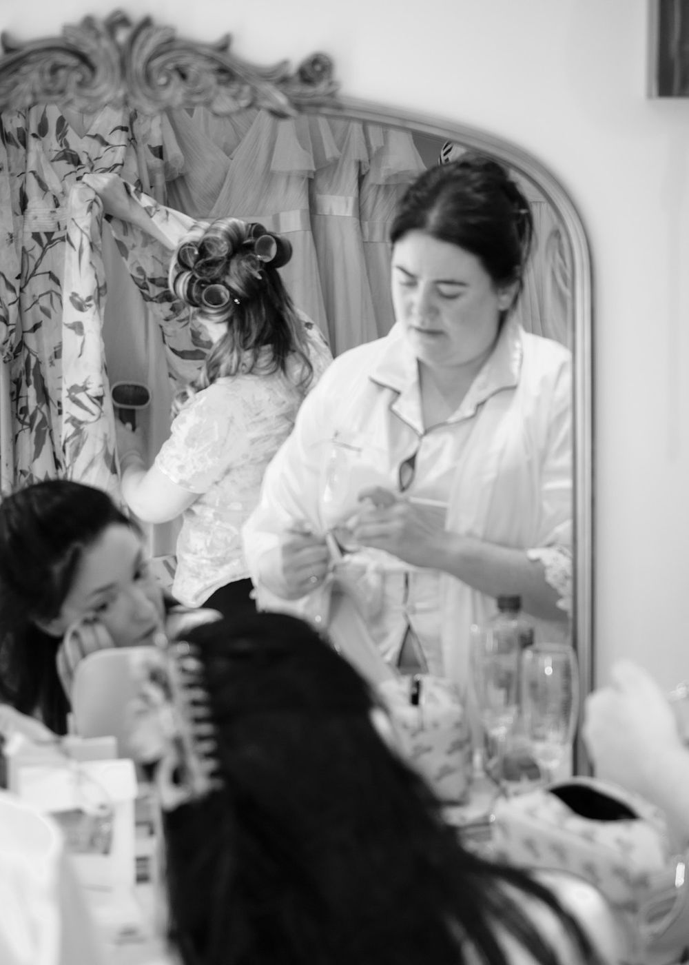 Black and white photo of bridesmaids getting ready in mirror-reflected dressing room.