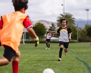 Young boys playing soccer on a green field, with one child in a white jersey dribbling the ball.