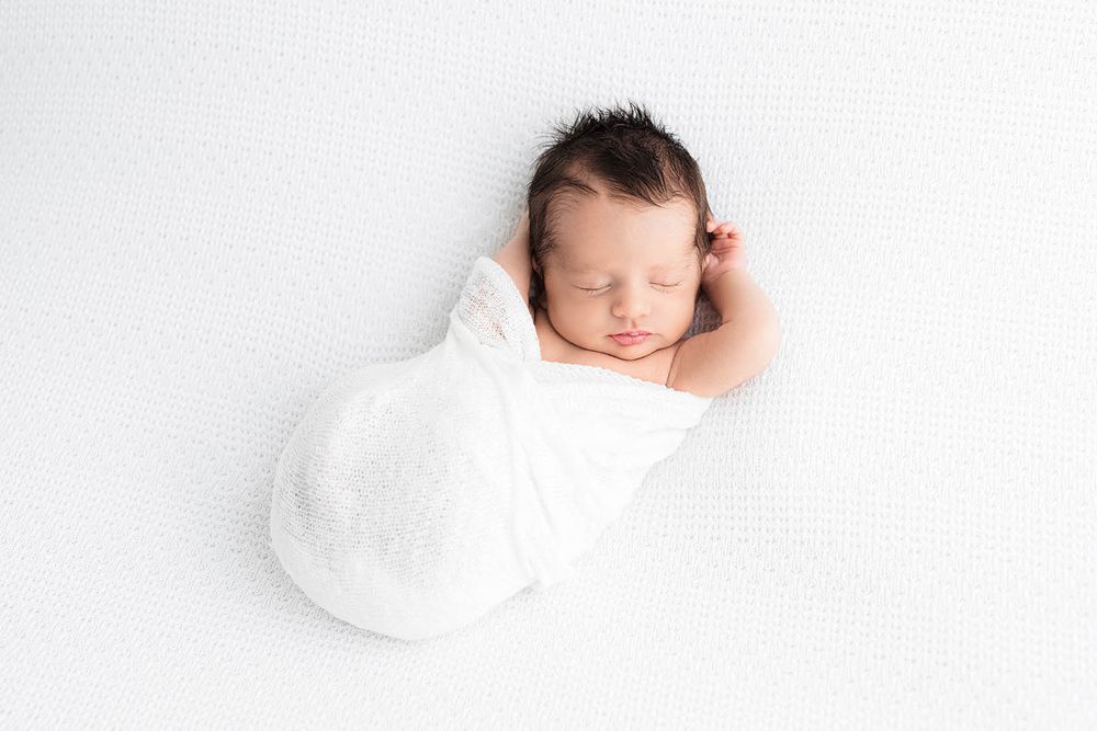 Newborn baby swaddled in white wrap sleeping on white background in professional studio photo by Menifee newborn preemie photographer.
