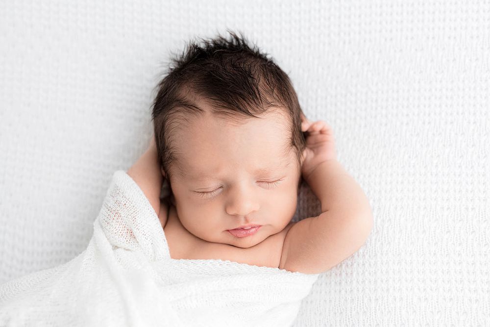 Peaceful newborn baby sleeping wrapped in white, with dark hair by Menifee newborn preemie photographer.
