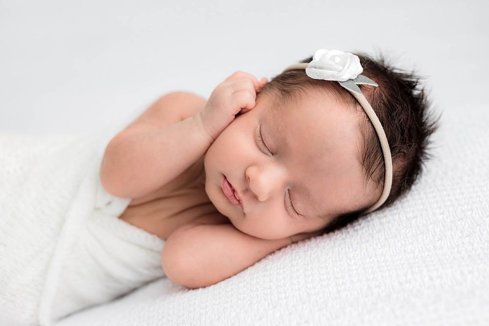 Peaceful newborn baby girl with dark hair sleeping on a white blanket by Menifee newborn preemie photographer.