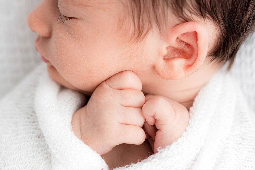 Close-up of a sleeping newborn baby with tiny fists tucked under chin by Menifee newborn preemie photographer.