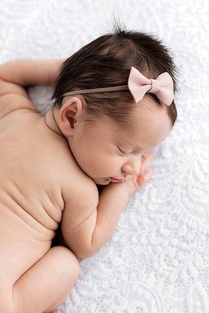 Sleeping newborn baby girl with dark hair wearing a pink bow headband by Menifee newborn preemie photographer.