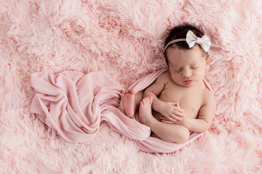 Sleeping newborn baby girl wrapped in pink on a fluffy pink background by Menifee newborn preemie photographer.