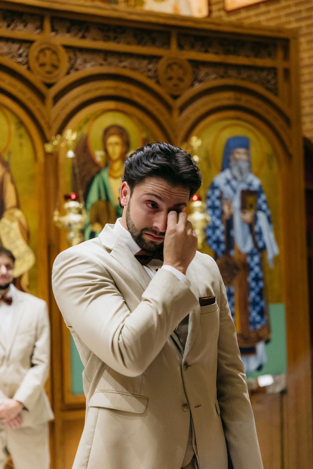 Emotional groom in cream suit wiping tears in Orthodox church during wedding ceremony in Chicago