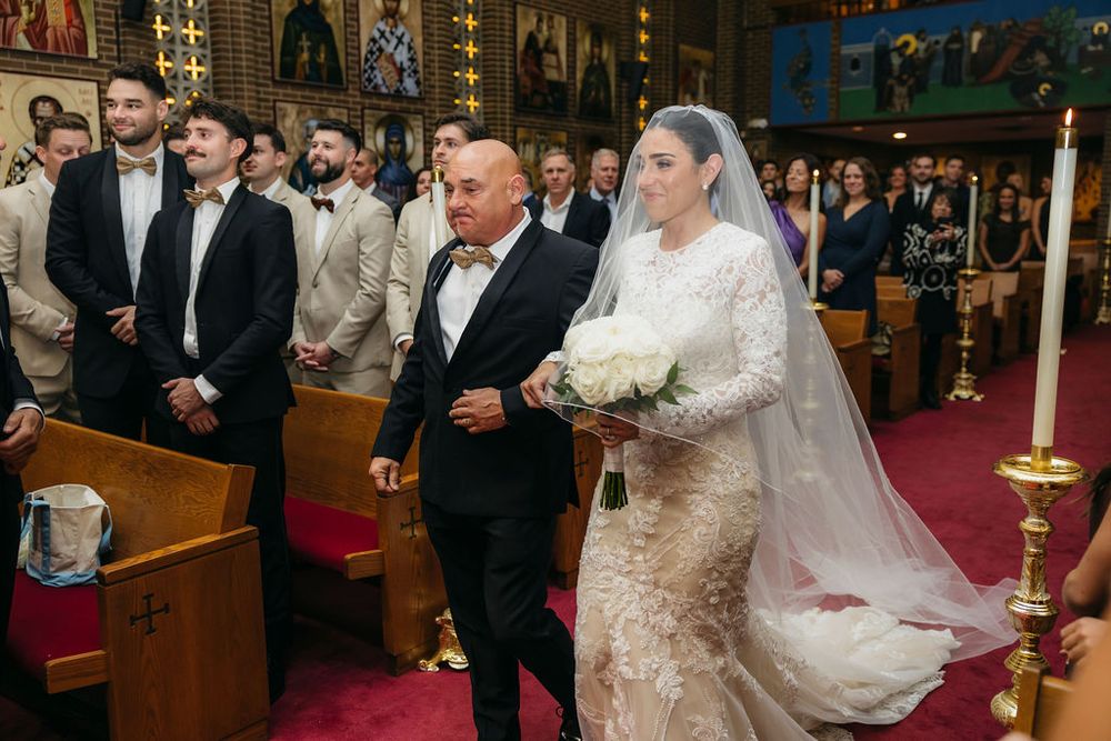 Bride in lace wedding gown walks down church aisle with father during traditional wedding ceremony in Chicago