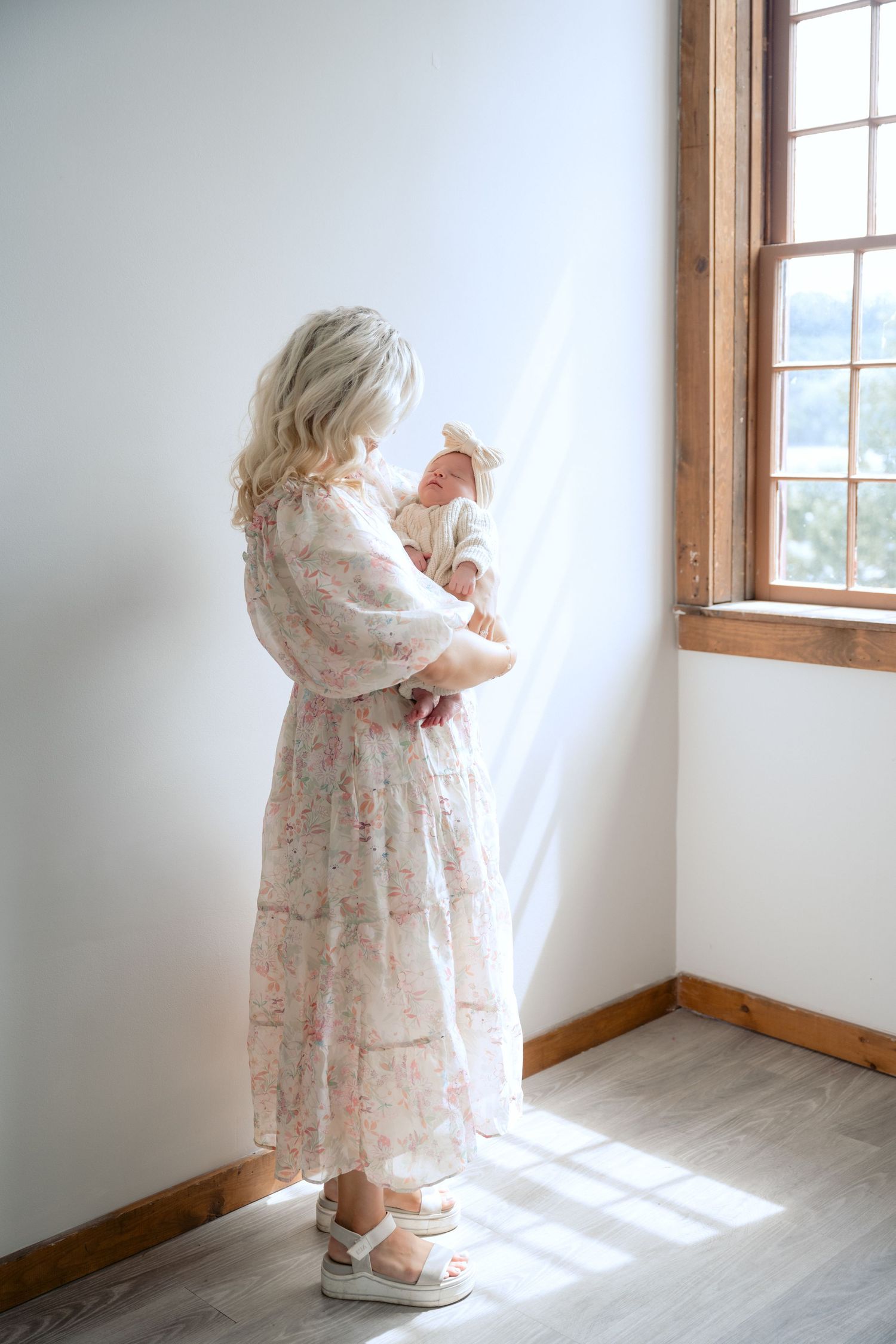 mom standing holding baby as the light from a nearby window illuminates them during in studio lifestyle newborn session in stillwater, mn